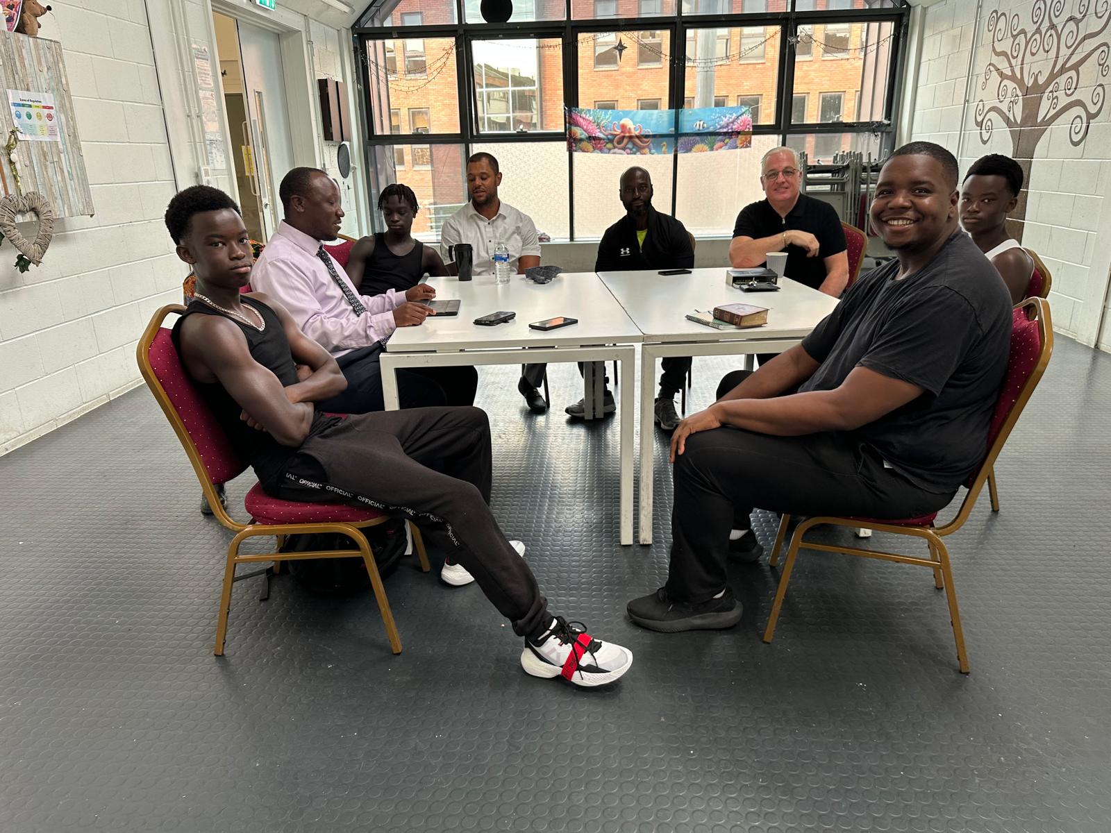 Members of the church family sitting together around a table in the Community House, laughing and talking